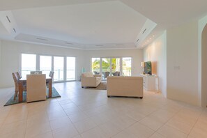 A spacious living room with a dining area, large windows, and a flat-screen TV. - Love Beach E2 - Luxury 3BR Condo + Pool & Beach (Nassau)