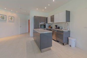 A modern kitchen with a central island, stainless steel appliances, and a white sink. - Love Beach E2 - Luxury 3BR Condo + Pool & Beach (Nassau)