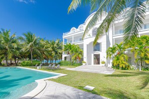 Un resort moderno con piscina, palmeras y un amplio edificio blanco con balcones.