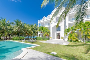 A modern resort with a pool, palm trees, and a large white building with balconies. - Love Beach E3 | 3BR Luxury Condo + Pool & Beach (Nassau)