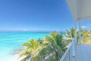 A balcony with a view of turquoise ocean and palm trees. - Love Beach E3 | 3BR Luxury Condo + Pool & Beach (Nassau)