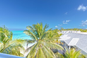 A coastal view with a clear sky, turquoise sea, and palm trees. - Love Beach E3 | 3BR Luxury Condo + Pool & Beach (Nassau)