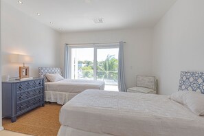 Ein Schlafzimmer mit zwei Betten, einem Schminktisch, einer Lampe und Blick ins Freie durch ein großes Fenster.
