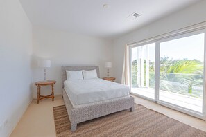 A bedroom with a large window, a bed with white bedding, two bedside tables, and a woven floor rug. - Love Beach E3 | 3BR Luxury Condo + Pool & Beach (Nassau)