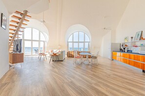 A spacious living area with a high ceiling, a staircase, and a kitchen with orange cabinets. - Love Beach E4 - 2BR Top-Floor Penthouse (Nassau)