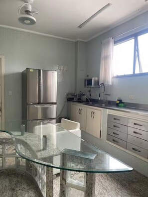 A kitchen with a glass-top table, stainless steel appliances, and a window with curtains. - Luxury - 5 suites - Pitangueiras - 80m from the beach - 2 parking spaces - R. Mário Ribeiro, 4 (Guarujá)