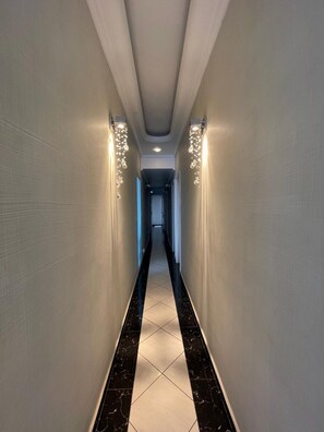 A corridor with a tiled floor, walls with a textured finish, and wall-mounted lighting fixtures. - Luxury - 5 suites - Pitangueiras - 80m from the beach - 2 parking spaces - R. Mário Ribeiro, 4 (Guarujá)