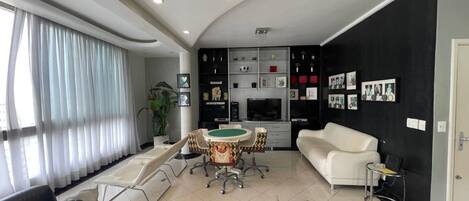 Una sala de estar moderna con un sofá blanco, una mesa de comedor con sillas, un televisor y una zona de cocina.