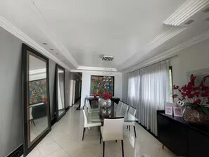 A modern dining area with a glass table and chairs, a large mirror, and a painting on the wall. - Luxury - 5 suites - Pitangueiras - 80m from the beach - 2 parking spaces - R. Mário Ribeiro, 4 (Guarujá)
