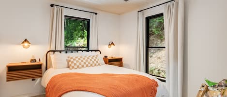 Quarto com cama, duas mesas de cabeceira, ventoinha no teto e janelas com cortinas.