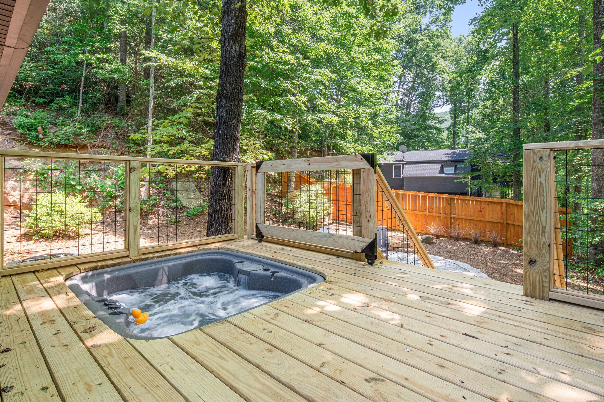 A wooden deck with a hot tub surrounded by a wooden fence and trees.