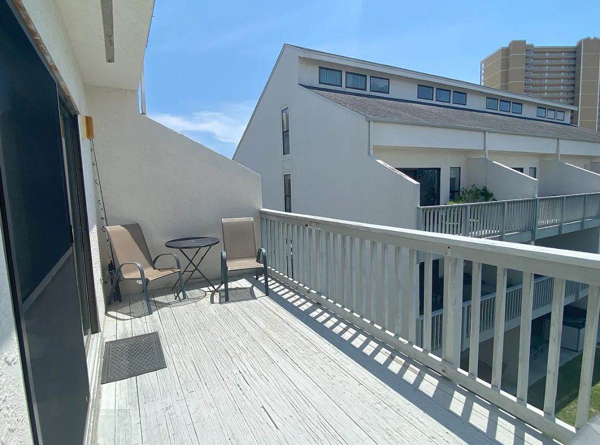 Ein Balkon mit weißem Geländer, einem kleinen Tisch und zwei Stühlen.