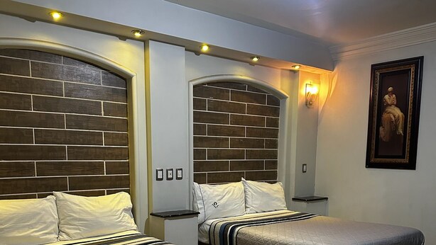 A hotel room with two beds, a brick-patterned headboard, a nightstand, a wall-mounted light, and a framed picture. - Hotel kristal (La Barca)