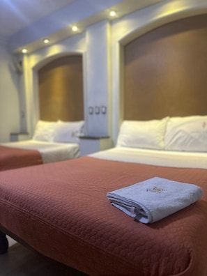 Habitación de hotel con dos camas, cada una con cabecero y almohadas. Hay una toalla doblada sobre la cama en primer plano.
