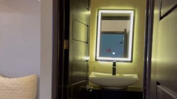 Una habitación de hotel con una cama, un baño con un espejo y un lavamanos, y una puerta que da a otra habitación.