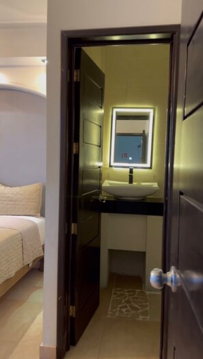 A hotel room with a bed, a bathroom with a mirror and sink, and a door leading to another room. - Hotel kristal  (La Barca)