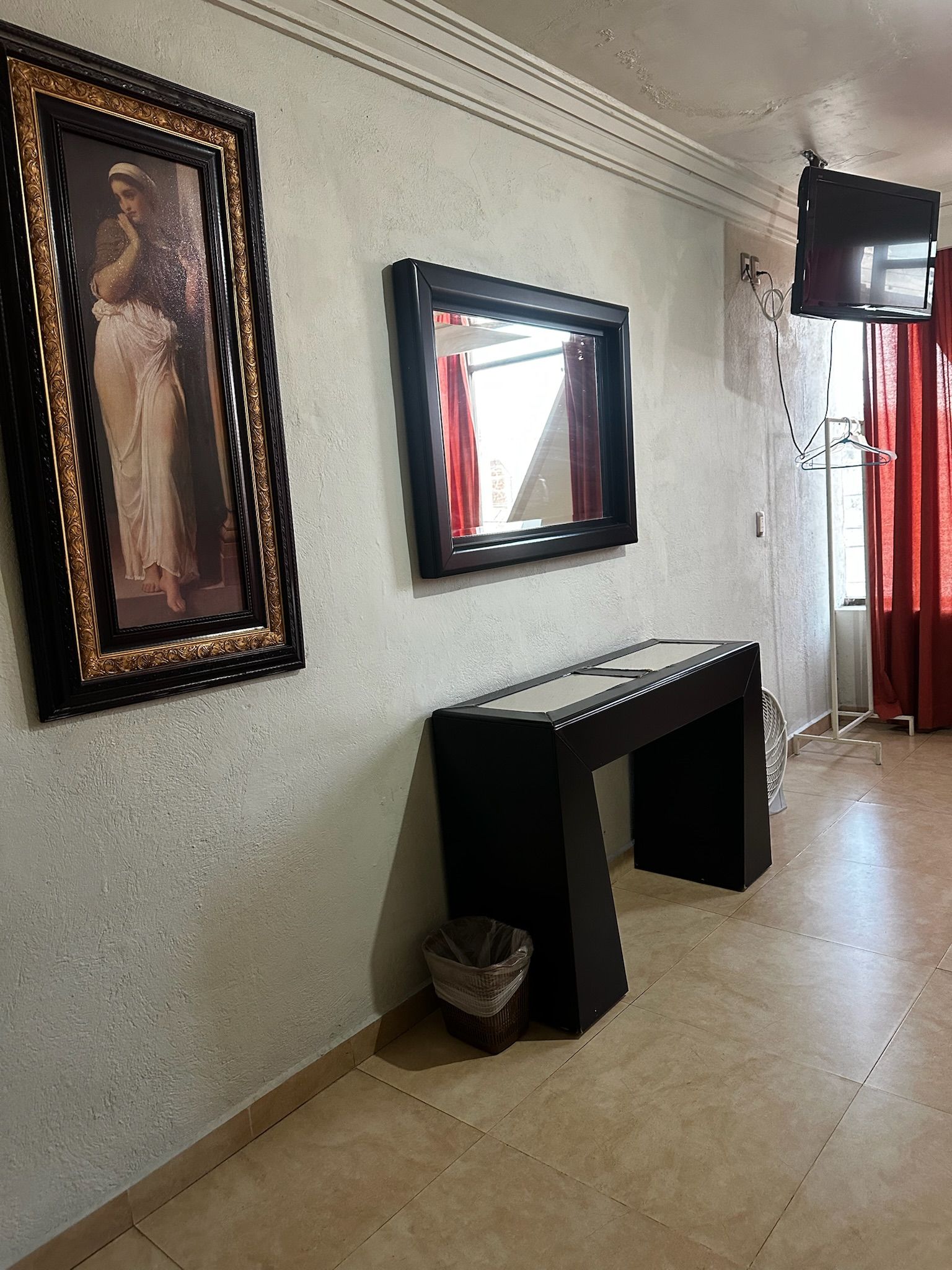 A room with a large framed painting, a mirror, a black console table, and a television mounted on the wall.