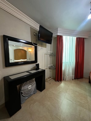 A hotel room with a flat-screen TV mounted above a black console, a large mirror, a fan, a glass shower enclosure, and red curtains. - Hotel kristal  (La Barca)
