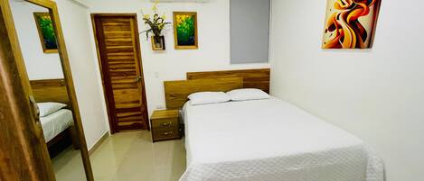 A bedroom with a bed, a bedside table, a mirror, a wall-mounted air conditioner, and a window.
