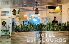 A reception area with a wooden counter, hanging pendant lights, and a large sign reading 'HOTEL ESI SEGUROS'.