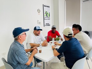 A group of people seated around a table in a room with a whiteboard and a poster on the wall.
