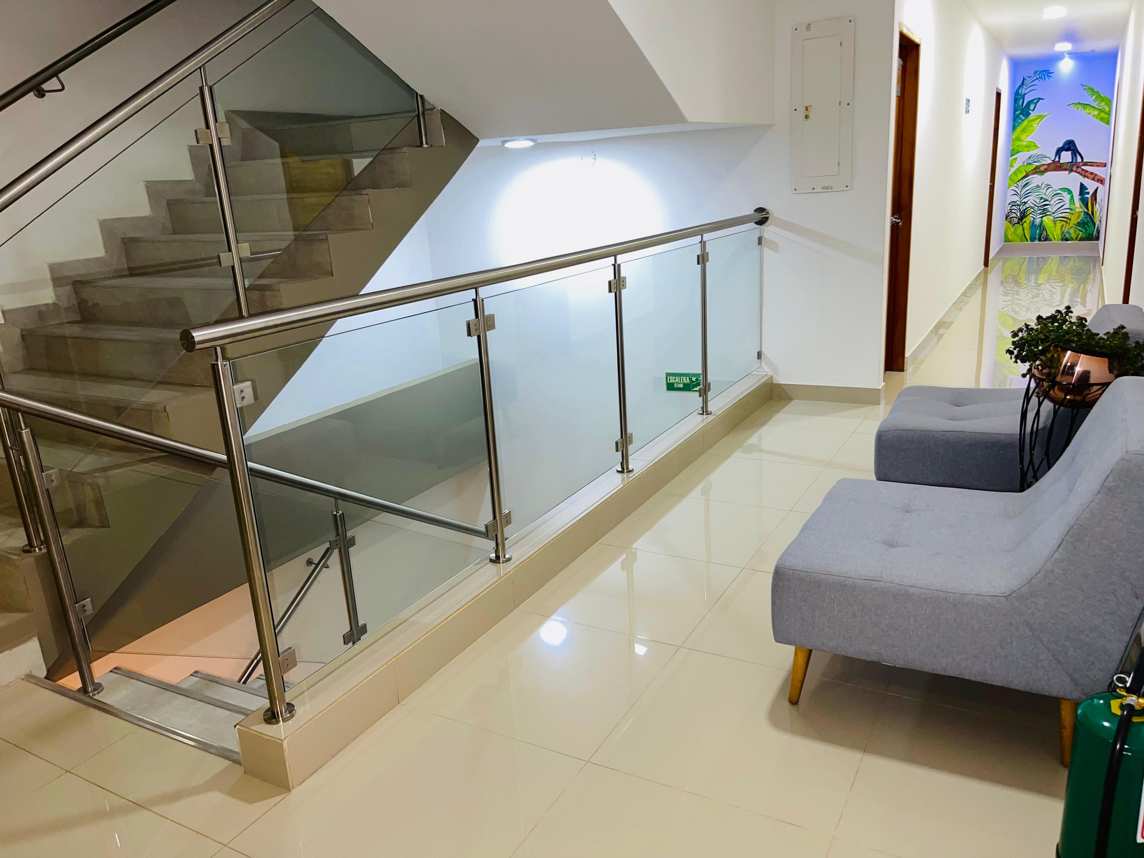 A modern interior with a glass staircase, a grey sofa, and a green fire extinguisher.