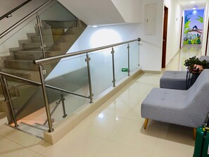 A modern interior with a glass staircase, a grey sofa, and a green fire extinguisher.