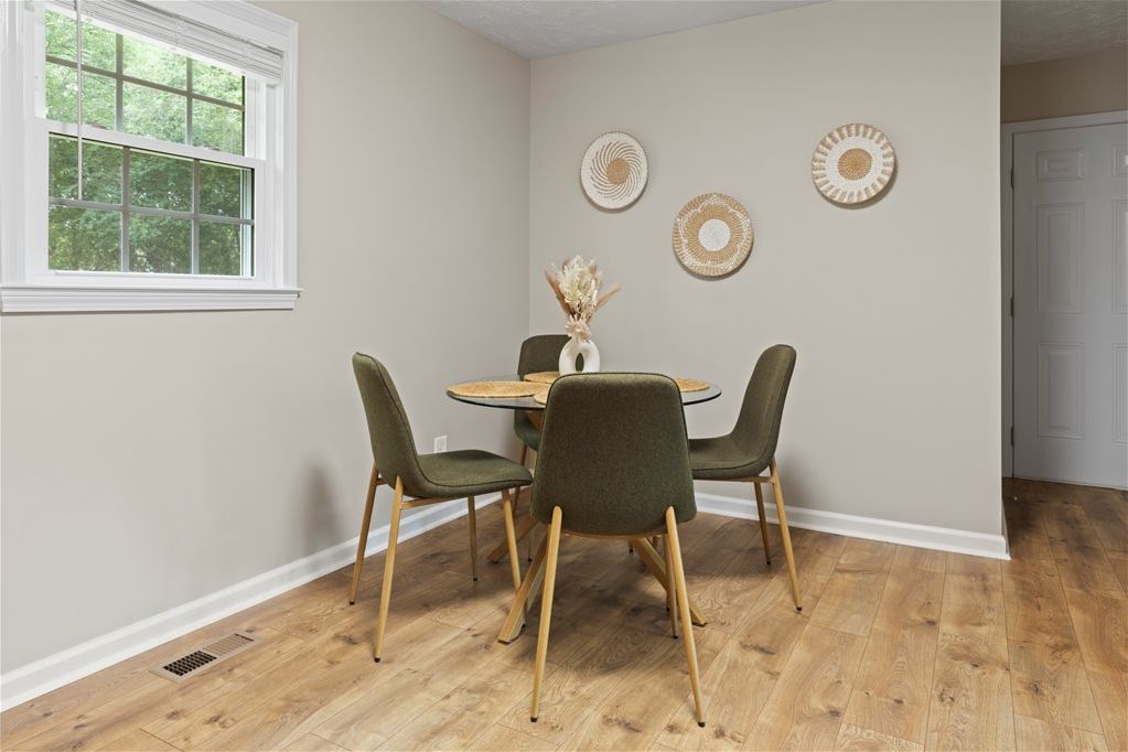 A dining area with a round table, four chairs, and decorative wall art.