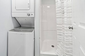 A compact bathroom with a washing machine, a shower stall, and a door with a striped pattern. - Saratoga Unit 10 minutes to everything! (Ballston Spa)