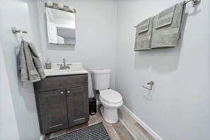 A small bathroom with a dark wooden vanity, a white toilet, and a towel rack. - Saratoga Unit 10 minutes to everything! (Ballston Spa)