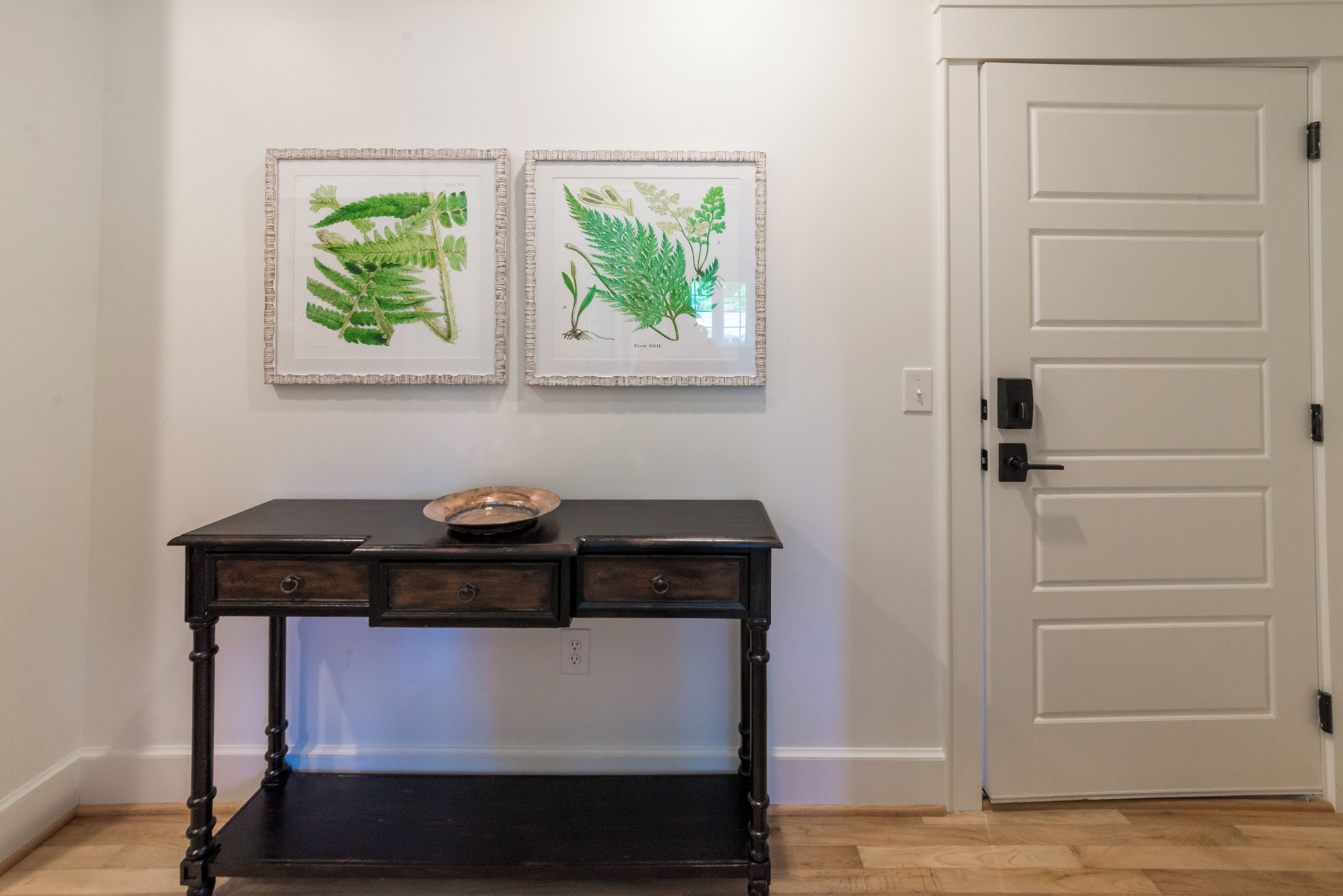 A room with a wooden console table, two framed botanical illustrations, and a white door.
