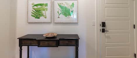 A room with a wooden console table, two framed botanical illustrations, and a white door.