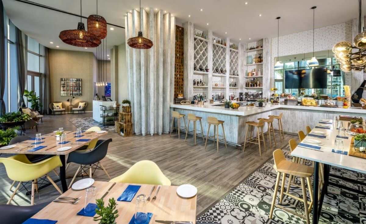 A modern hotel lobby with a bar area, seating arrangements, and a large window.
