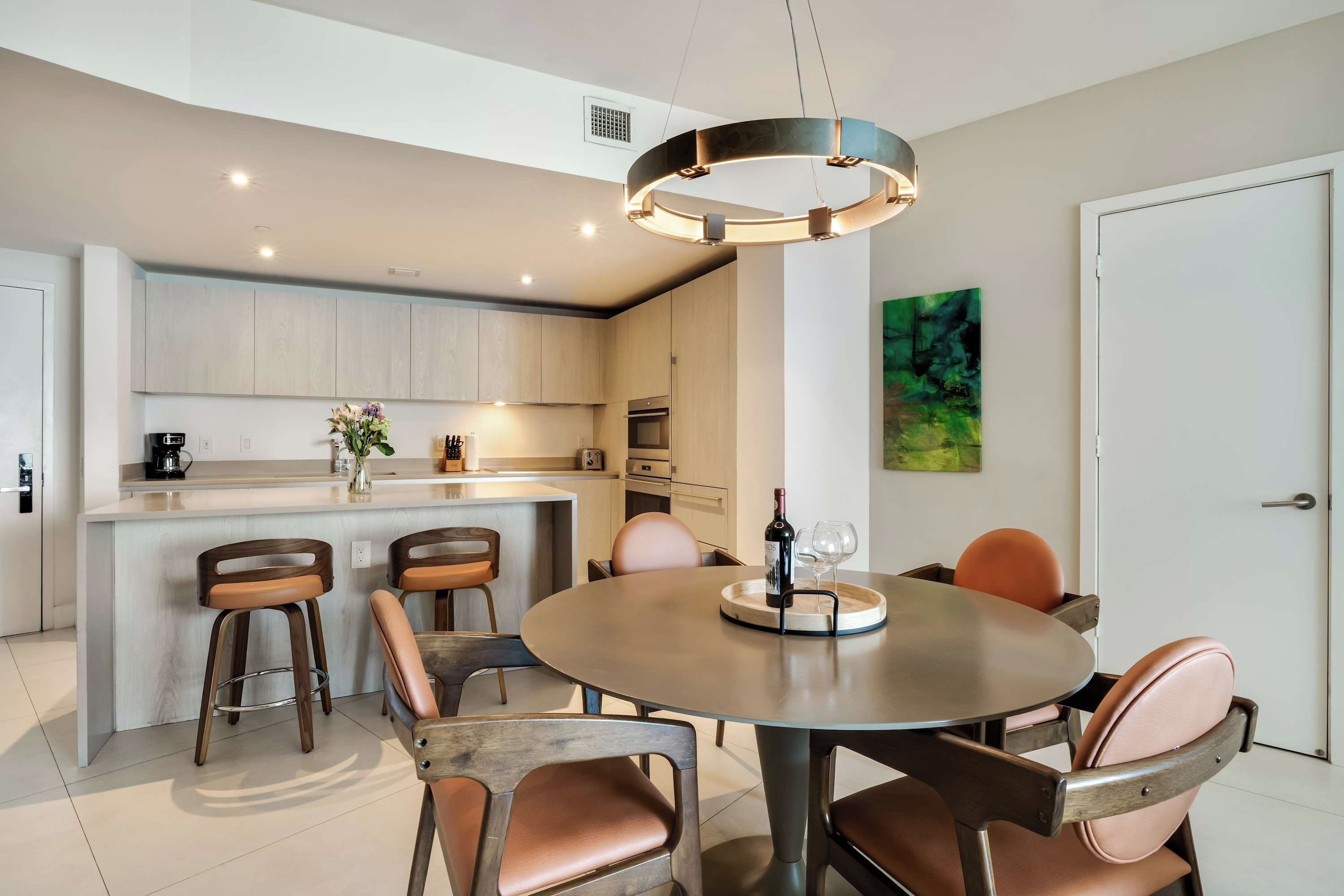 A modern kitchen with a central island, bar stools, a round dining table, and a pendant light.