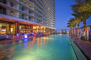 Un hotel de varios pisos con piscina, mobiliario exterior y palmeras.