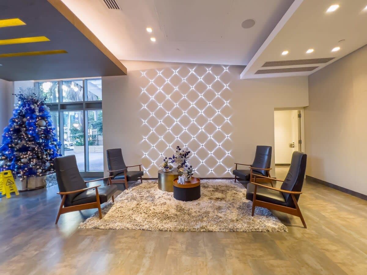 A lobby with four black chairs around a central coffee table, a Christmas tree, and a geometric light panel on the wall.