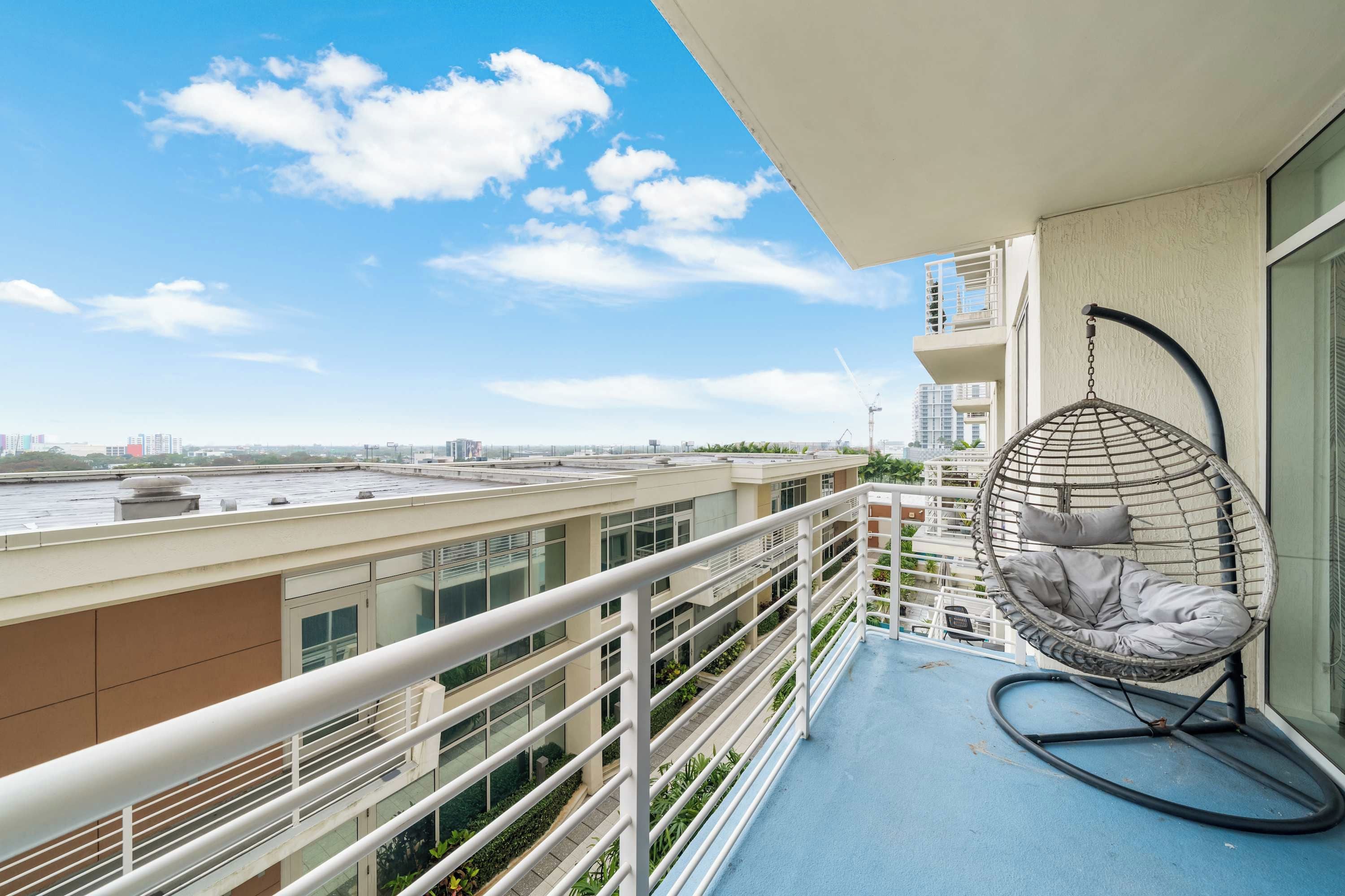 Un balcon avec un fauteuil suspendu, une balustrade et une vue sur le paysage urbain.