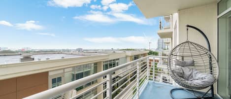 A balcony with a hanging chair, a railing, and a view of the cityscape.