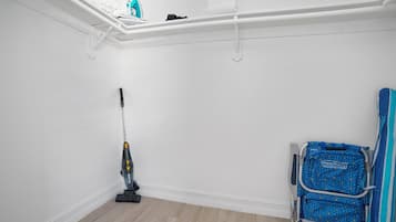 Ein Zimmer mit Staubsauger, blauem Stuhl und weißem Regal mit Gegenständen.