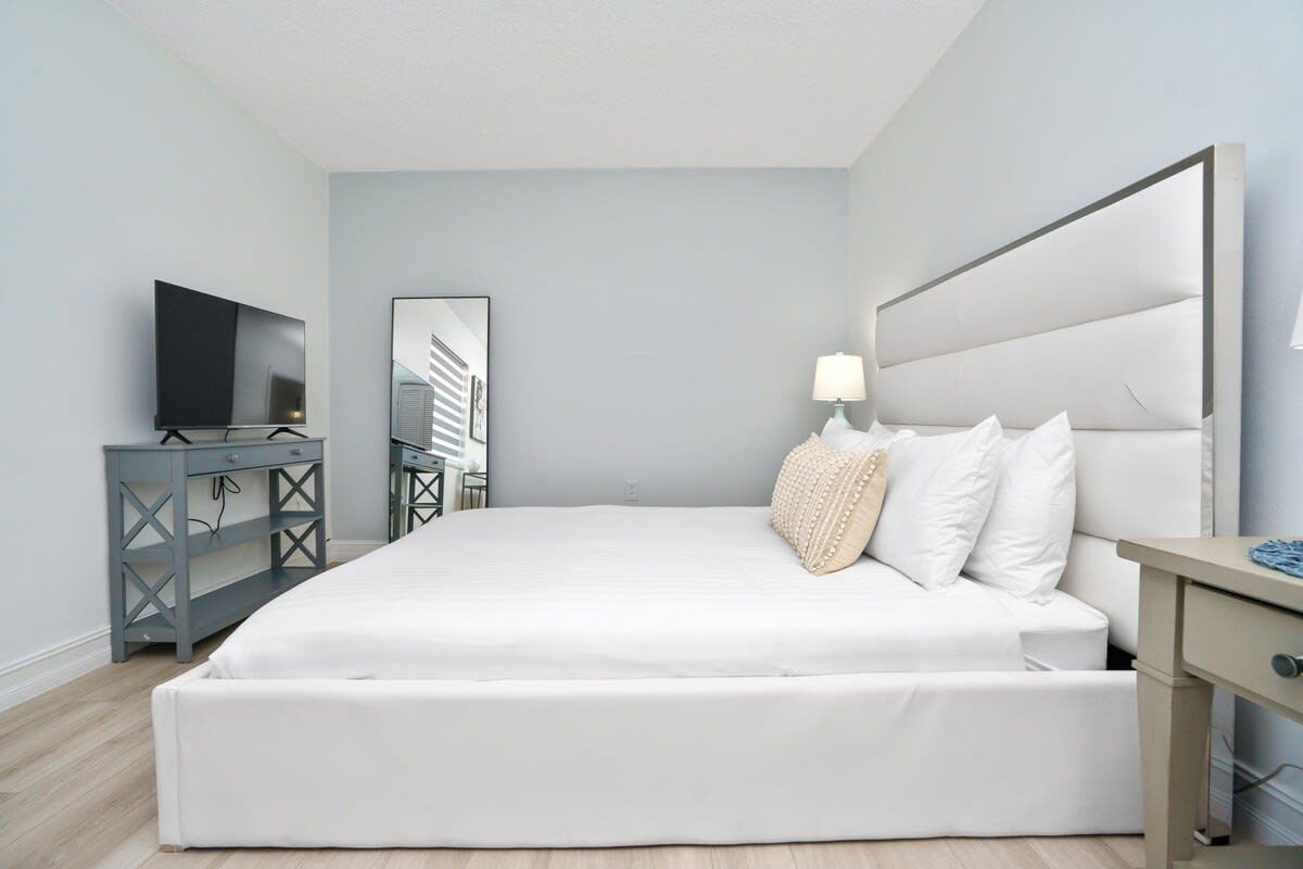 Quarto moderno com uma cama grande, televisão, escrivaninha e espelho.