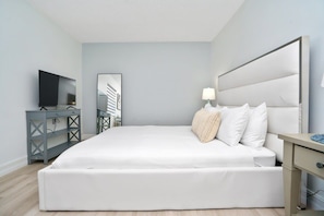 Quarto moderno com uma cama grande, televisão, escrivaninha e espelho.