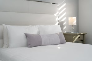 A neatly made bed with a headboard, a bedside table with a lamp, and a wall with a window casting shadows. - Cozy Blue Door Duplex, Central in Cutler Bay (Cutler Bay)