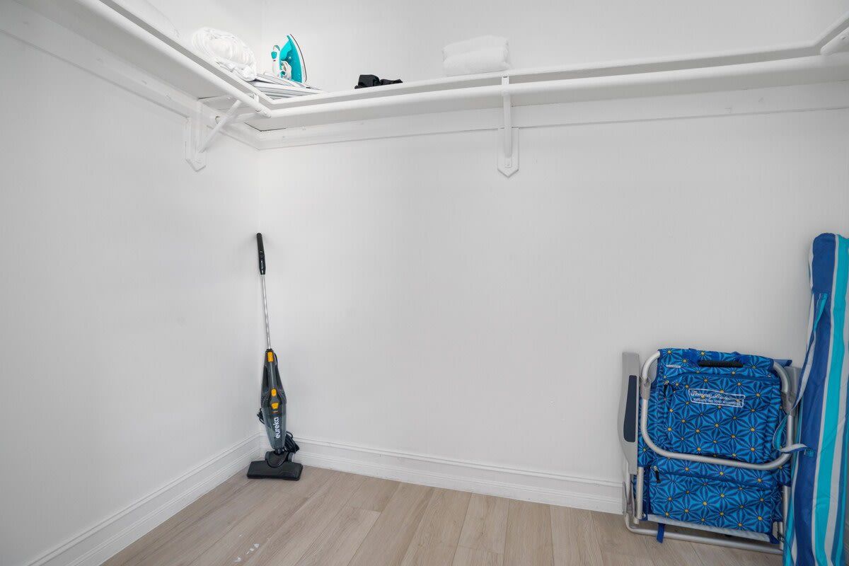 Una habitación con una aspiradora, una silla azul y una estantería blanca con objetos.