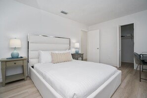 Quarto com cama, mesas de cabeceira, escrivaninha e uma cadeira.