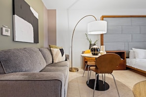 A modern hotel room with a grey sofa, a round dining table, a lamp, a bed, and a wall-mounted artwork. - Biscayne Bay Views Studio Central in Miami (Miami)