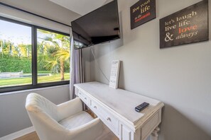 Una habitación con un escritorio blanco, una silla, un televisor montado y decoración motivacional en la pared.