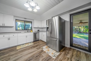 Una cocina moderna con armarios blancos, un refrigerador de acero inoxidable y ventana con vista a un jardín.