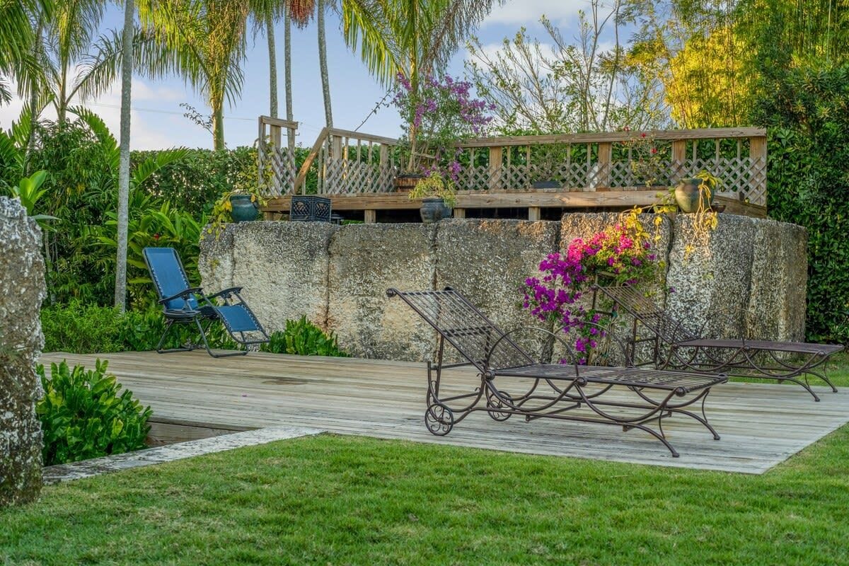 A garden patio with a wooden deck, a stone wall, and a metal bench.