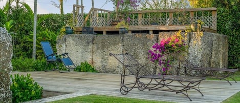 A garden patio with a wooden deck, a stone wall, and a metal bench.