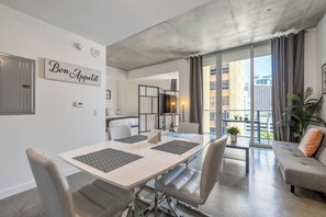 A modern living room with a dining area, a sofa, and a large window with curtains. - Charming Downtown Pad, Rooftop Pool in Miami (Miami)